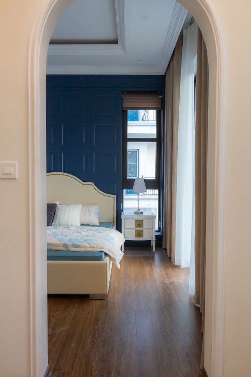 Free Elegant bedroom with blue accent wall and wooden flooring, viewed through a white archway. Stock Photo