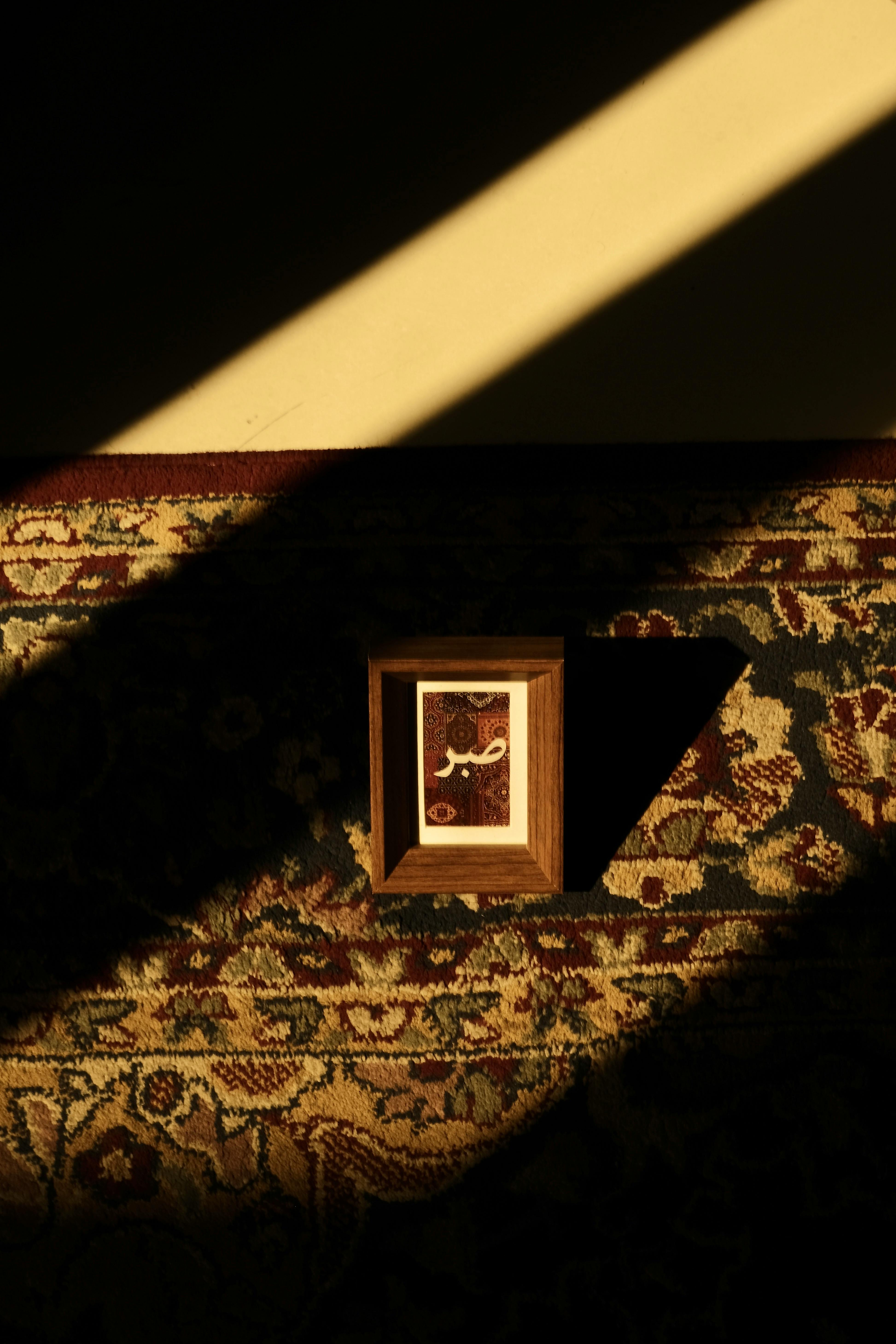 A wooden frame on a patterned carpet, illuminated by dramatic shadows.