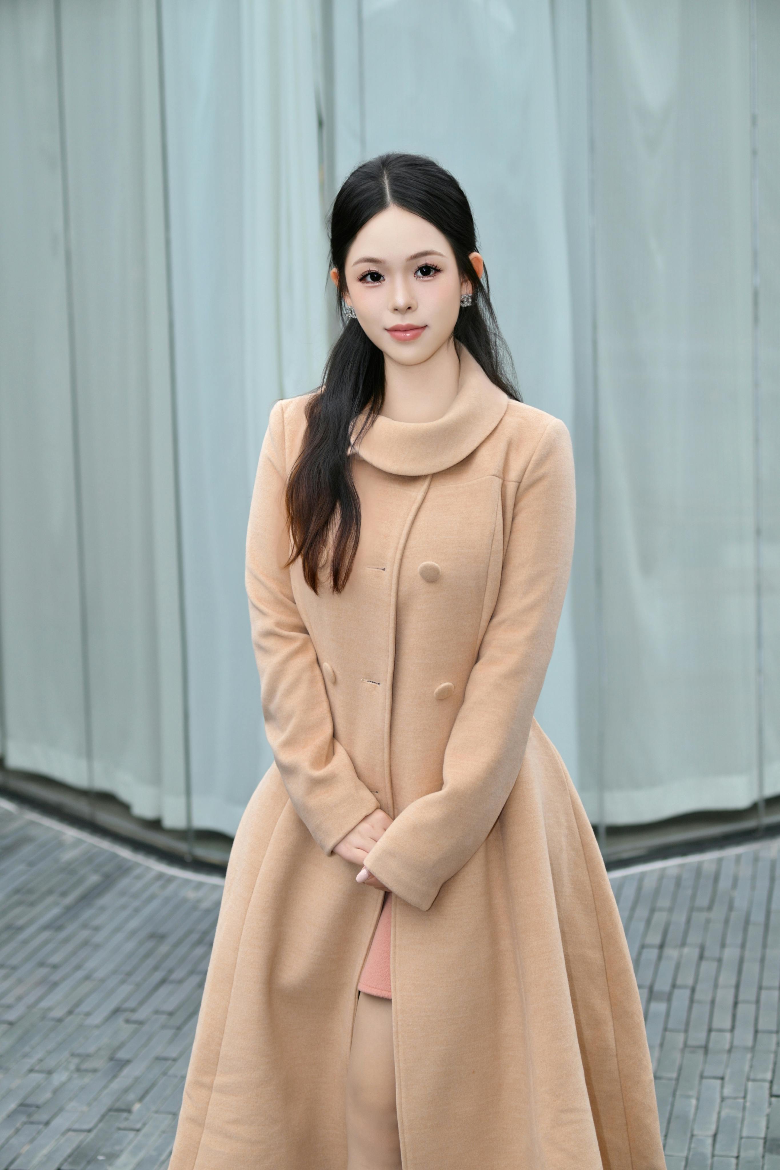 Portrait of a woman in a stylish tan coat standing outdoors with a cool backdrop.
