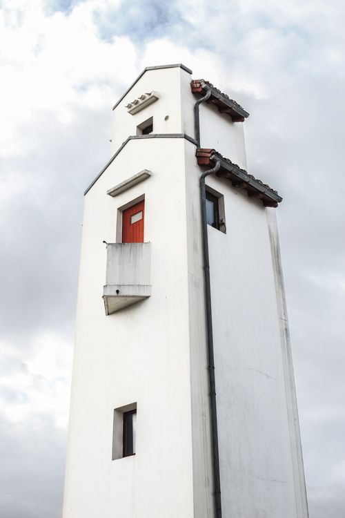 Free White tower with red door and windows under a cloudy sky, showcasing minimalism. Stock Photo