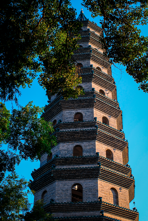 Free A beautiful brick pagoda surrounded by lush green trees against a clear blue sky. Stock Photo