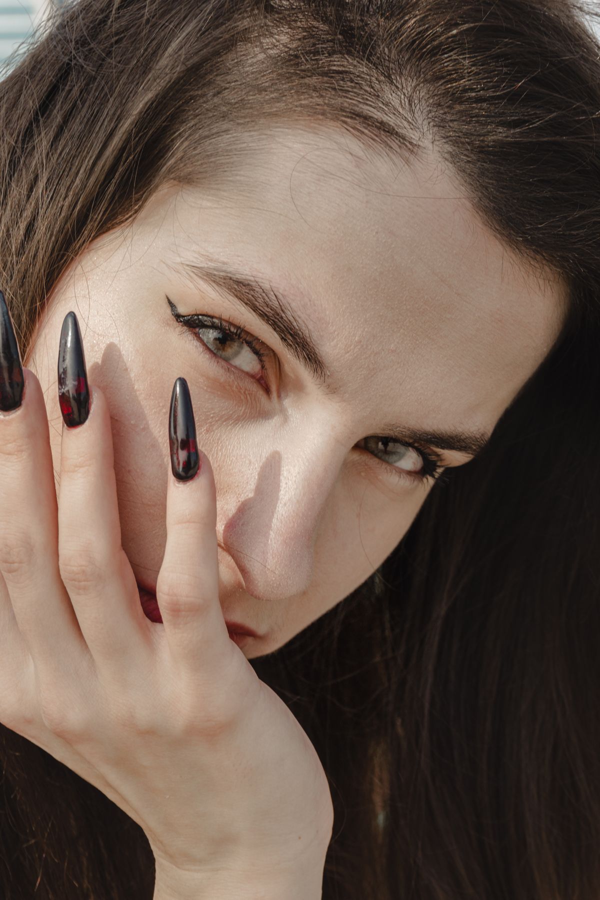 Intense close-up portrait of a woman showcasing gothic-style black nails and natural makeup.