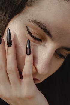 A striking close-up portrait highlighting dramatic eyeliner and stylish dark nails, showcasing modern beauty.