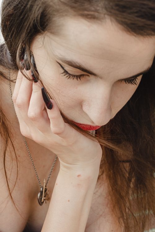 Free Close-up portrait of a woman with thoughtful expression, resting her chin on her hand. Natural outdoor lighting. Stock Photo