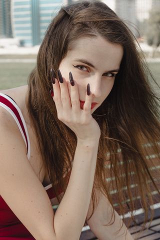 Close-up of a woman outdoors with long dark nails and thoughtful expression, captured in daylight.