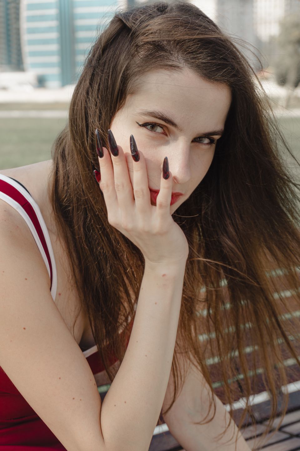 Close-up of a woman outdoors with long dark nails and thoughtful expression, captured in daylight.
