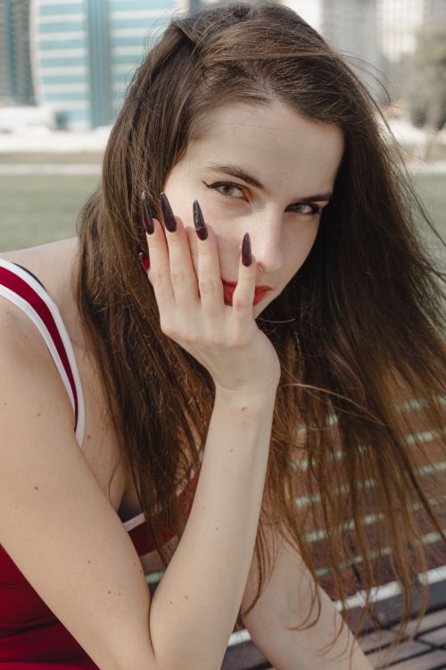 Free Close-up of a woman outdoors with long dark nails and thoughtful expression, captured in daylight. Stock Photo