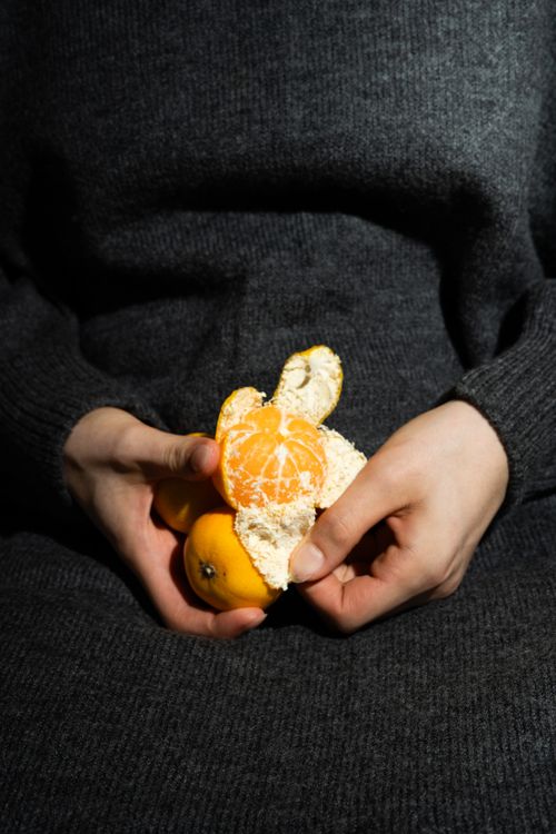 Free A person in a grey sweater peels a bright orange tangerine, showcasing its fresh and juicy segments. Stock Photo
