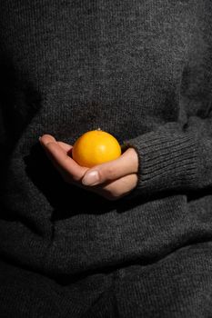 A contemplative image featuring a hand in a gray sweater holding a vibrant orange.