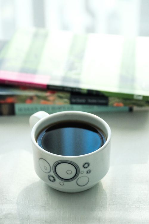 Free A uniquely designed coffee mug with books in background, basking in soft morning light. Stock Photo