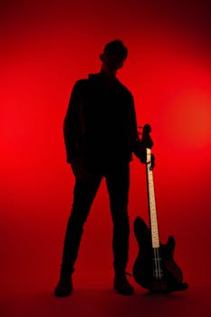 Silhouette of a male musician holding a bass guitar against a bold red background.