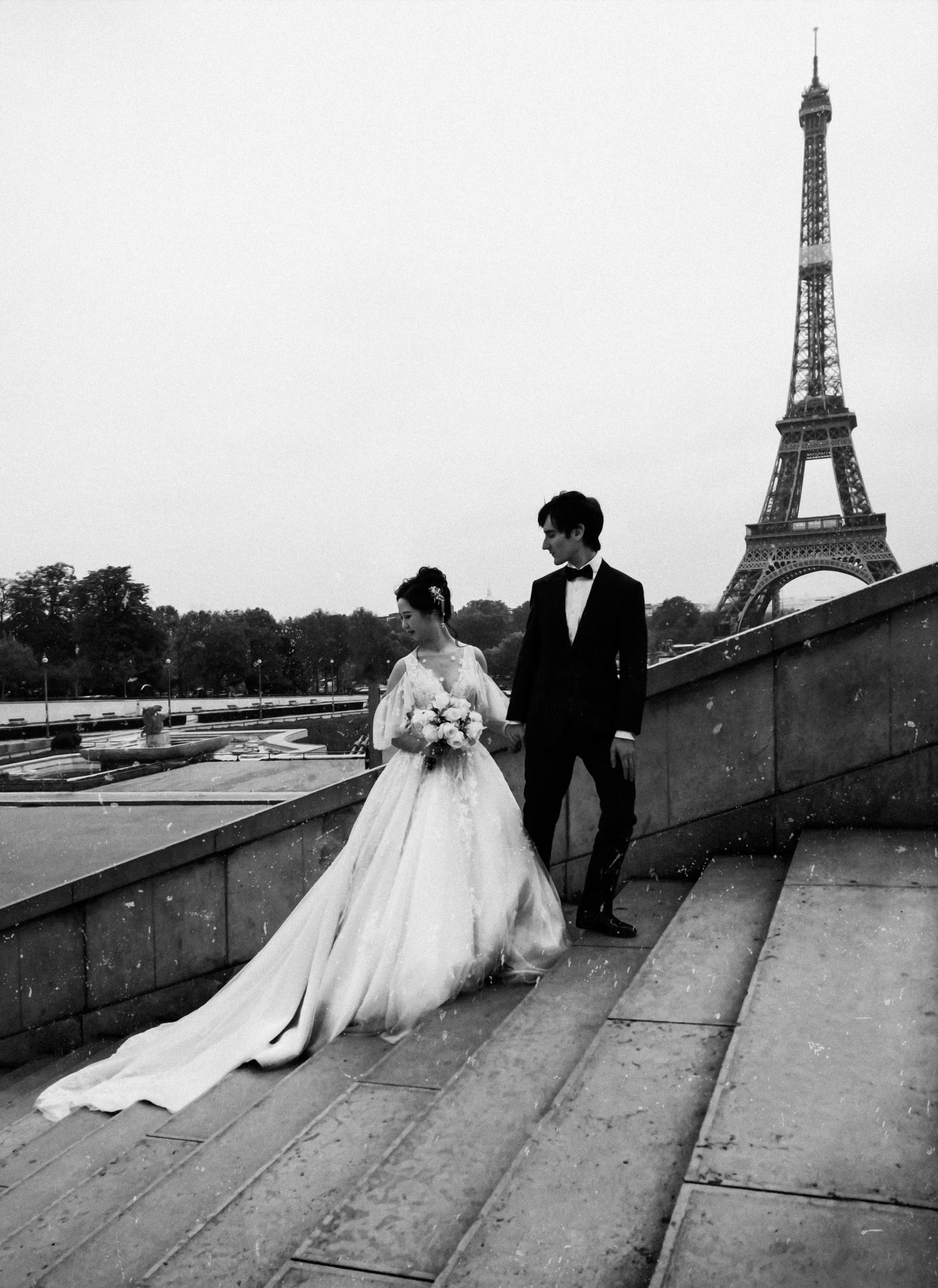 grayscale photo of bride and groom standing on concrete stairs