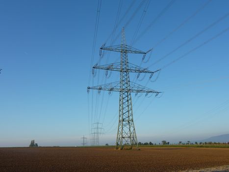 High voltage power lines on a tower standing in an open field against a clear blue sky.