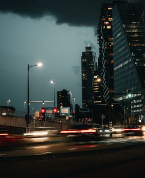 Dramatic night scene of a cityscape with skyscrapers and blurred car lights.