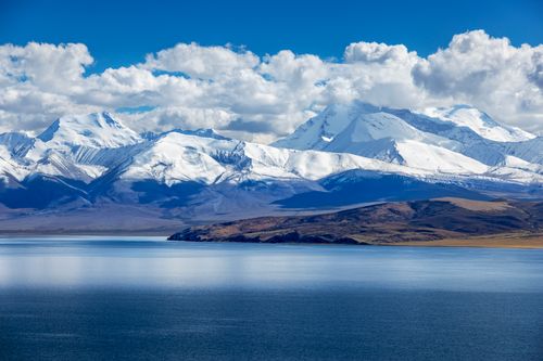 Free Breathtaking view of snow-covered mountains reflecting in a serene lake under a cloud-dotted sky. Stock Photo