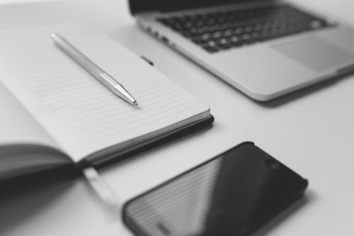 Free Black Iphone Beside Silver Pen on White Notebook Near Laptop Computer on Table Stock Photo