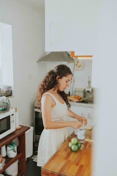 A young woman prepares food in a bright, modern kitchen, focusing on fresh ingredients and healthy cooking.
