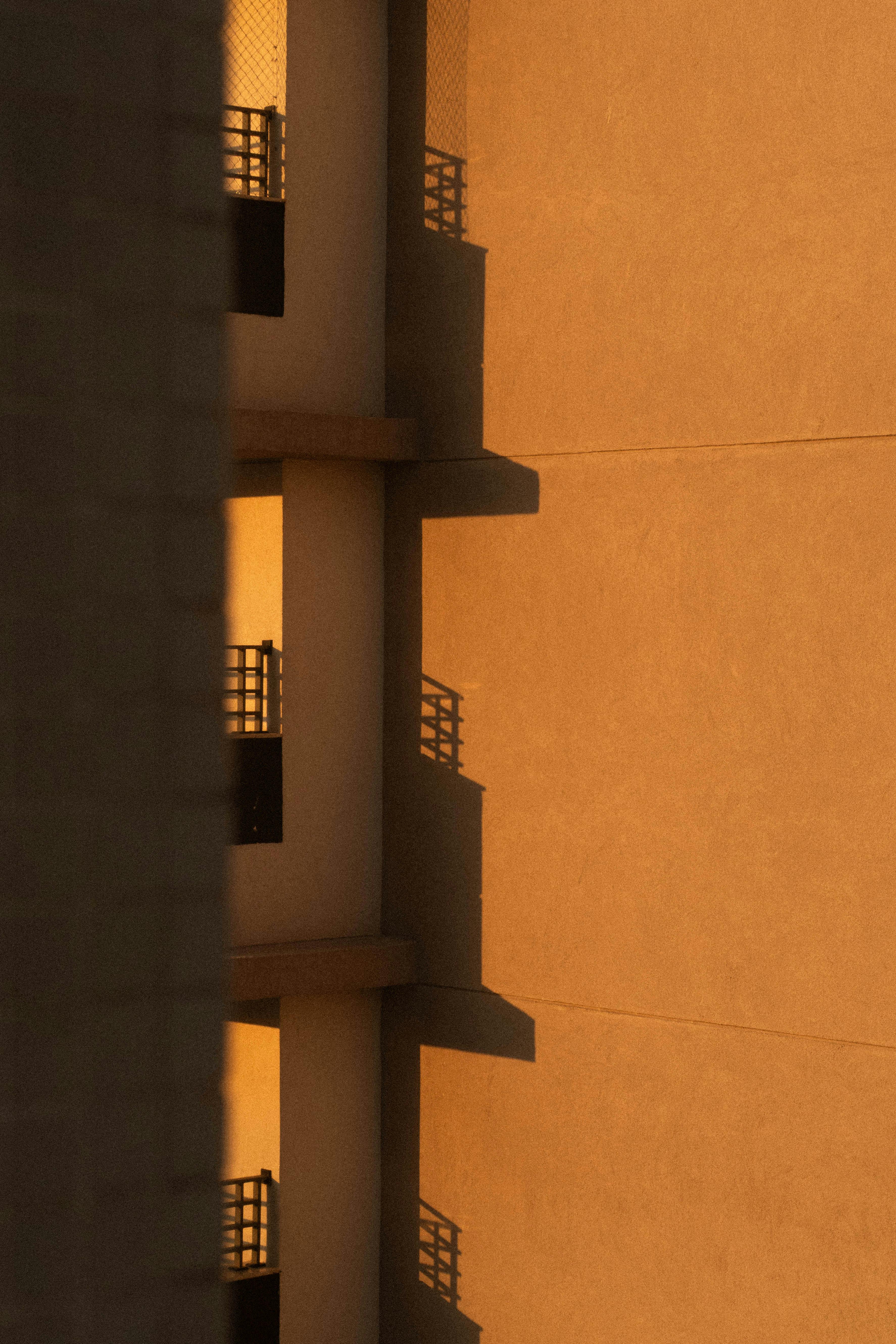 Gratis Una cálida puesta de sol proyecta sombras abstractas sobre la fachada de un edificio moderno, resaltando la arquitectura urbana. Foto de stock