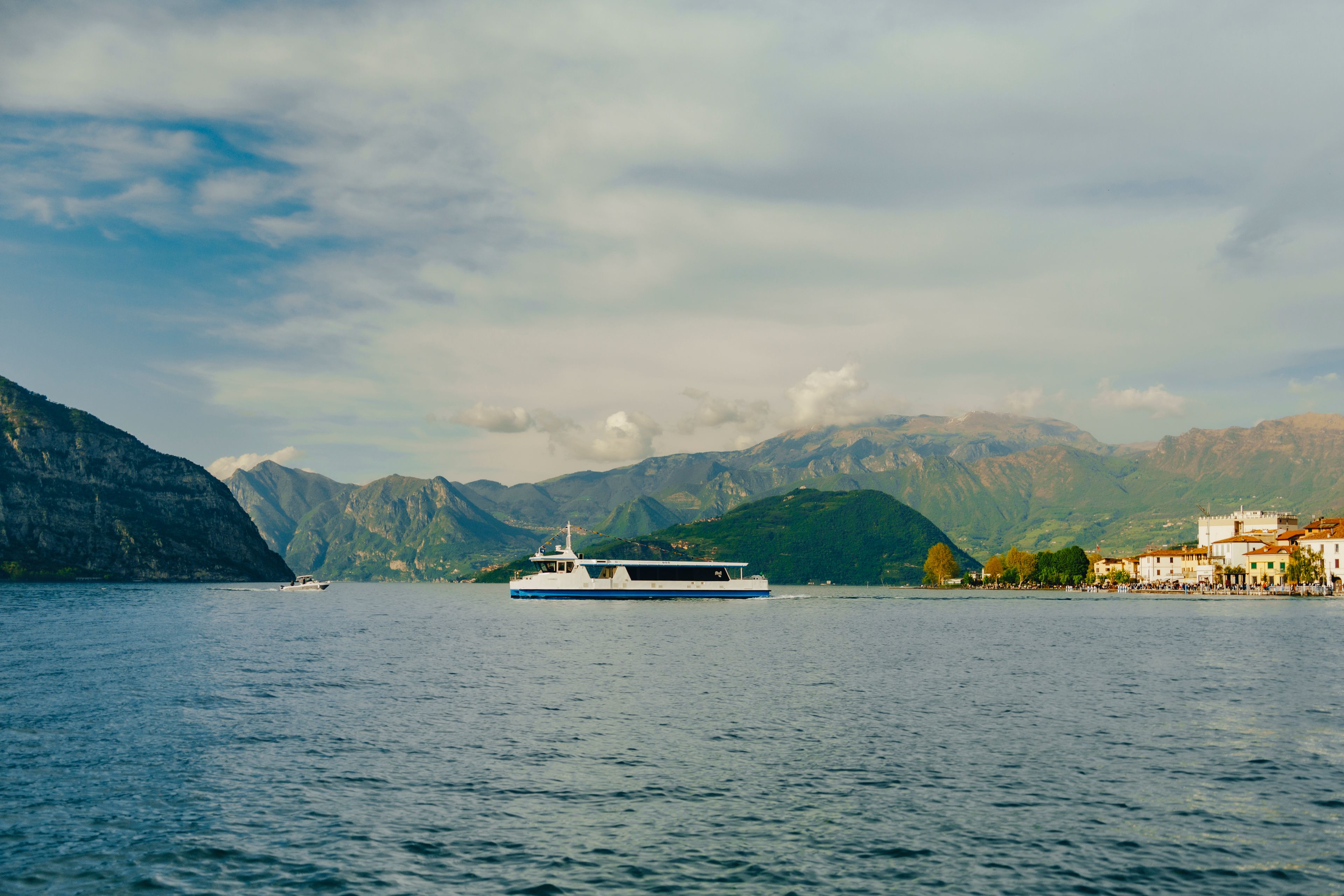 Tranquil scene of Lake Iseo with a boat, surrounded by mountains and picturesque Italian town.