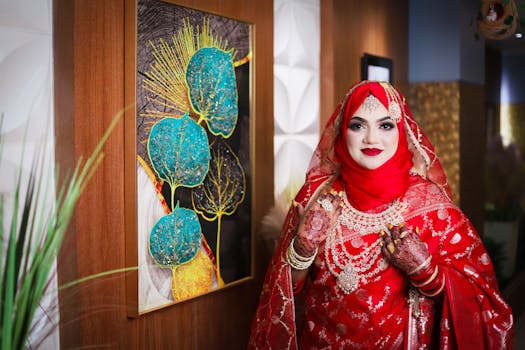 Asian bride in stunning red dress with intricate henna and jewelry indoors.