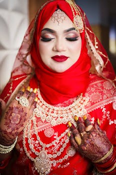 Elegant South Asian bride adorned in red and gold bridal jewelry with intricate henna.