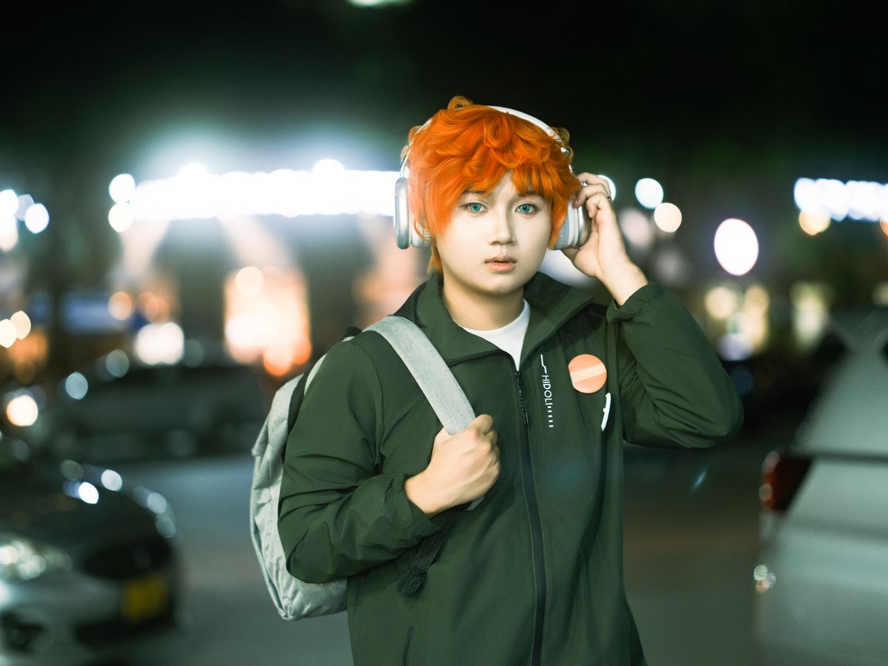young adult with striking orange hair and headphones in a nighttime ur