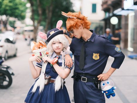 Cosplay couple dressed as animal characters from a popular Disney movie, posing outdoors with plush toys.