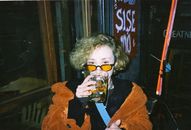 Person enjoys a drink at a cozy İzmir bar, wearing orange coat and glasses.