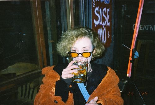 Free Person enjoys a drink at a cozy İzmir bar, wearing orange coat and glasses. Stock Photo