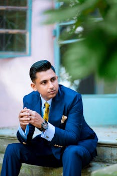 Young man in a blue suit sitting outdoors, exuding confidence and style.