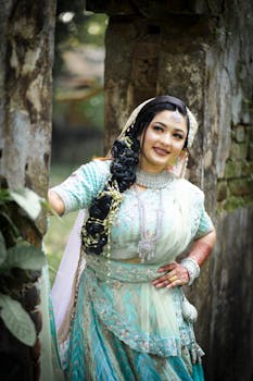 Beautiful bride in a turquoise lehenga posing outdoors with rustic architecture.