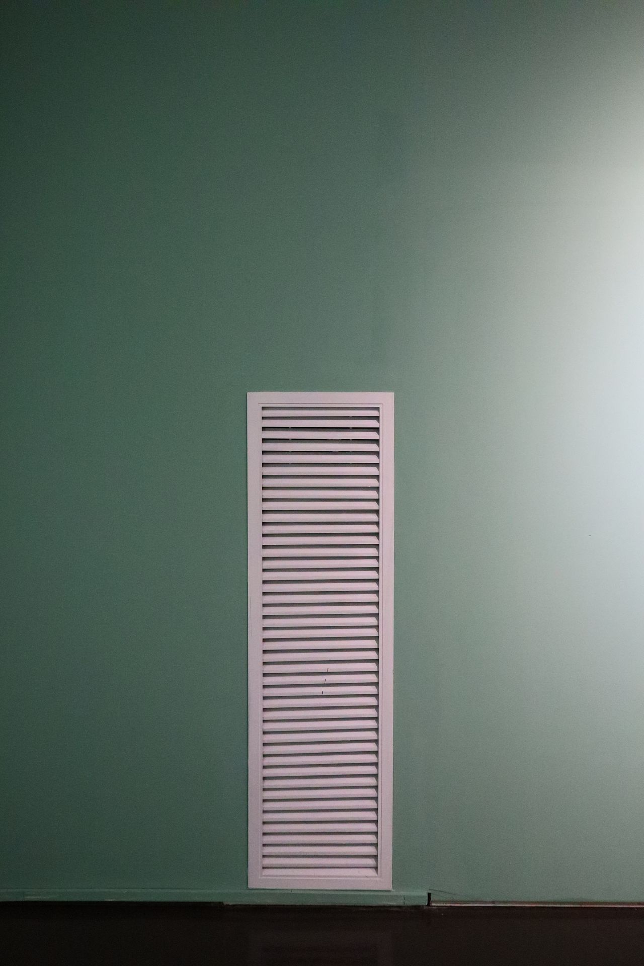 A white louvered vent on a mint green wall