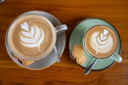 Two cups of latte art coffee with cookies on a wooden table in Bali, Indonesia.