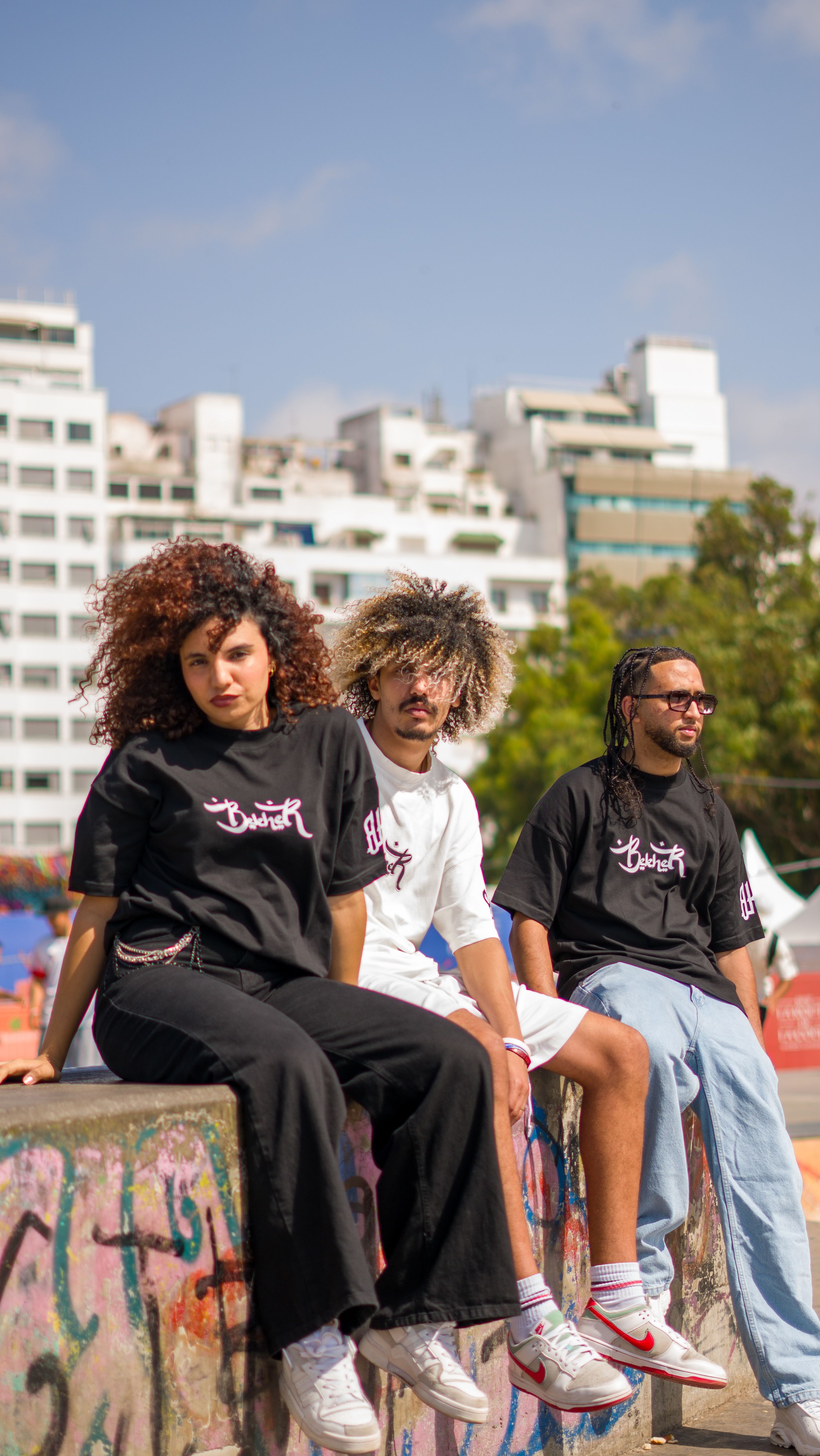Three stylish young adults sitting on a wall in a vibrant urban environment.