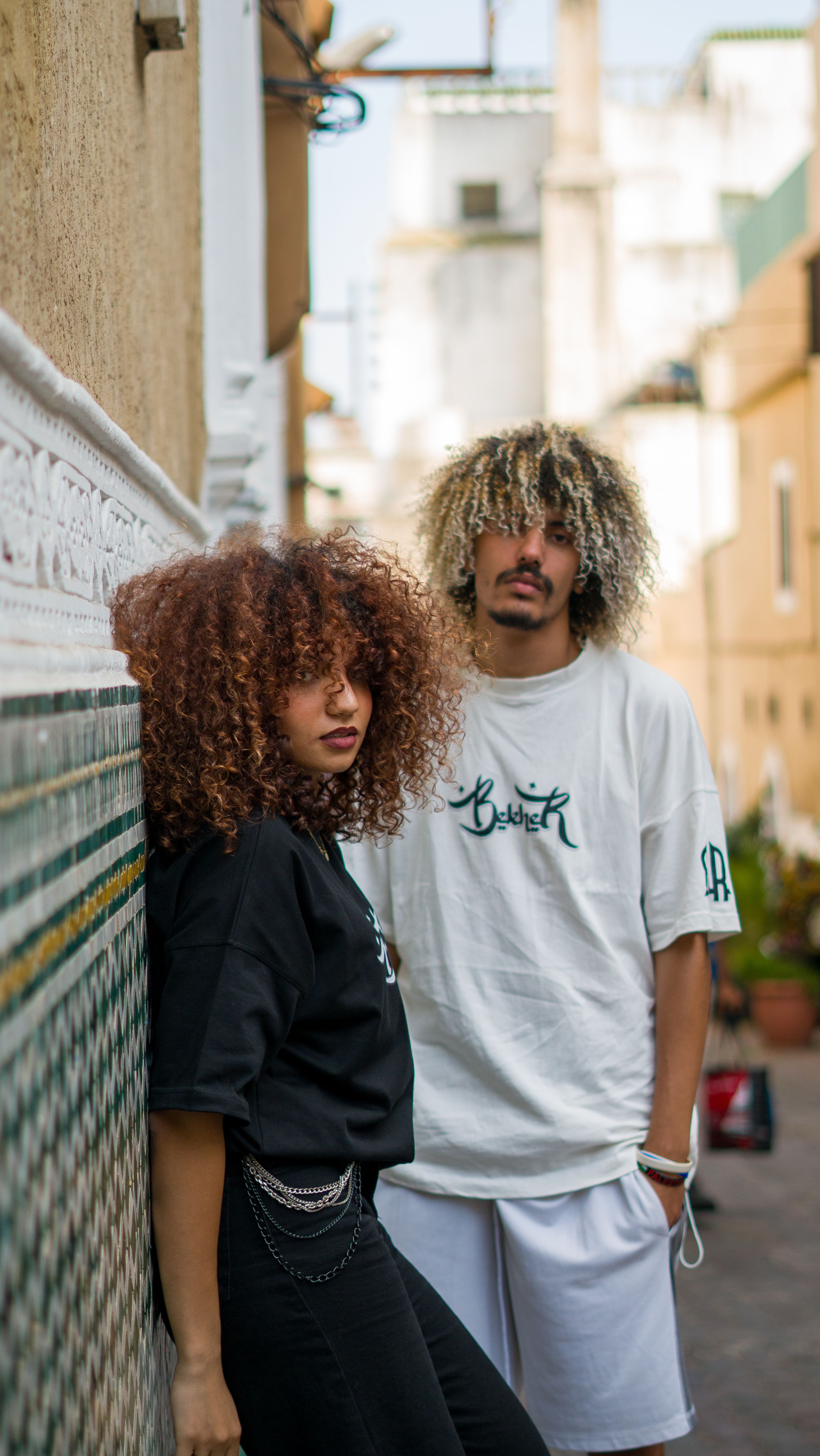 Two stylish adults posing in an urban setting with striking curly hairstyles.