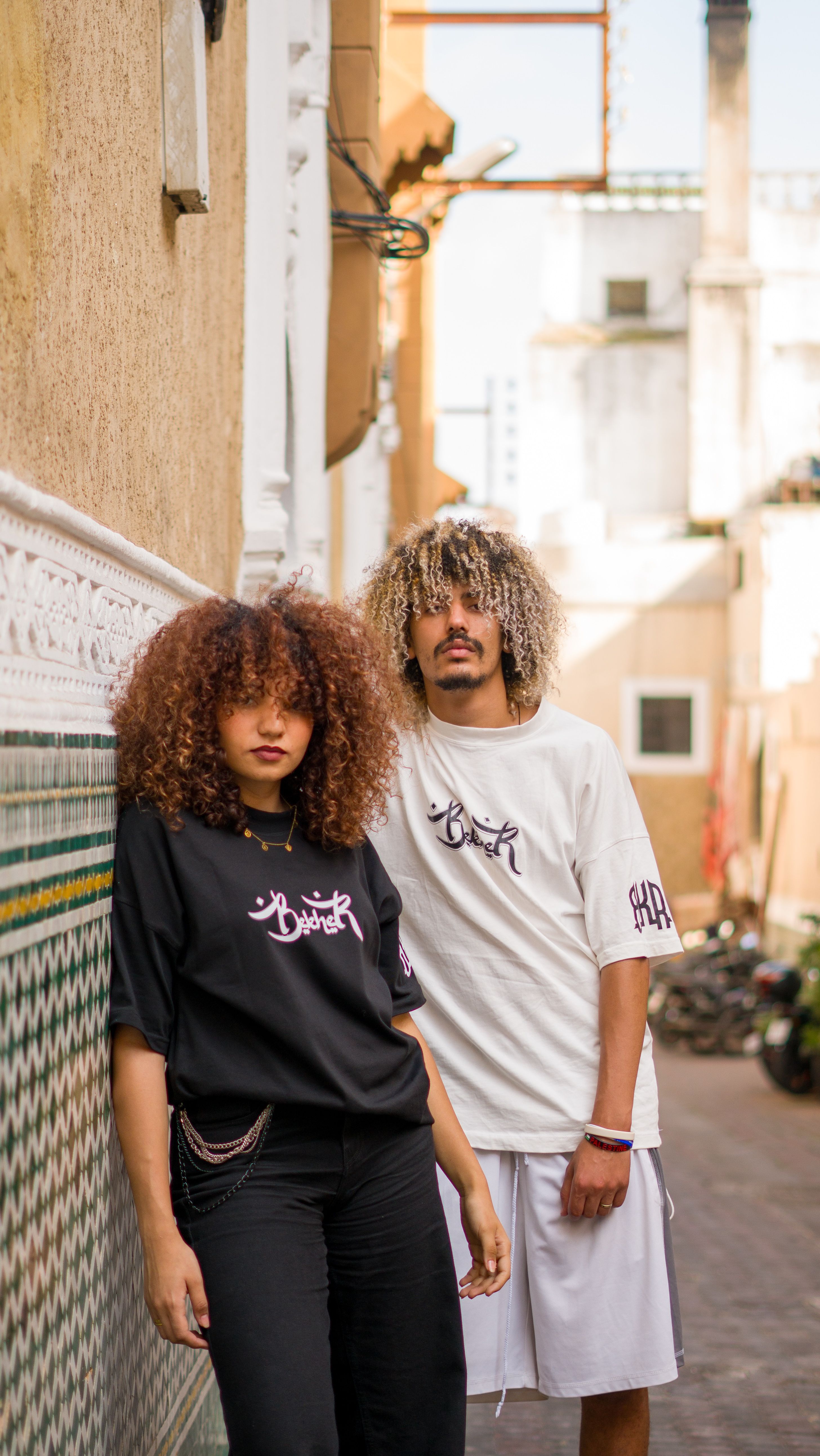 Stylish couple wearing matching outfits pose confidently in a vibrant urban alleyway, showcasing modern street fashion.