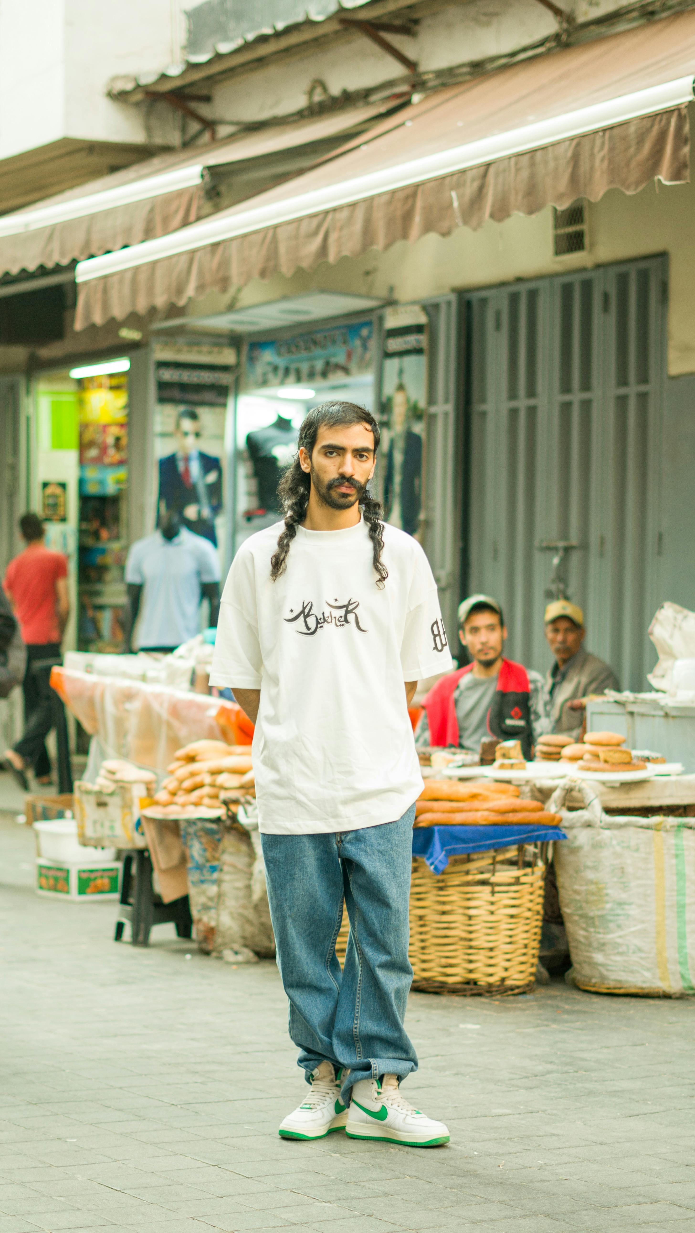 Stylish man in casual attire stands in a vibrant market in Morocco.