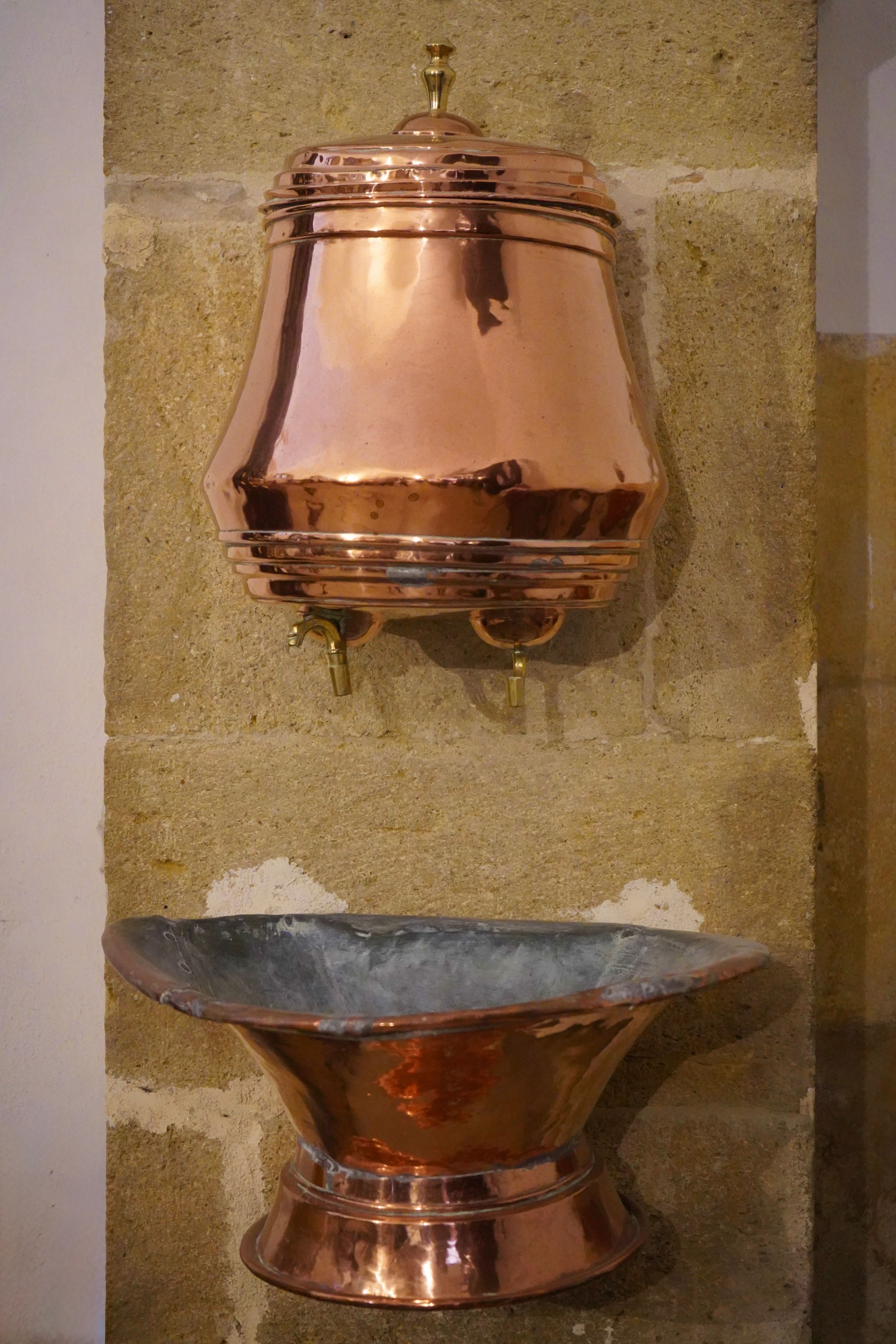 Copper water basin on rustic stone wall, reflecting traditional design.