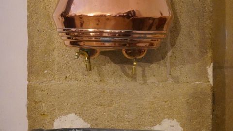 Copper water basin on rustic stone wall, reflecting traditional design.