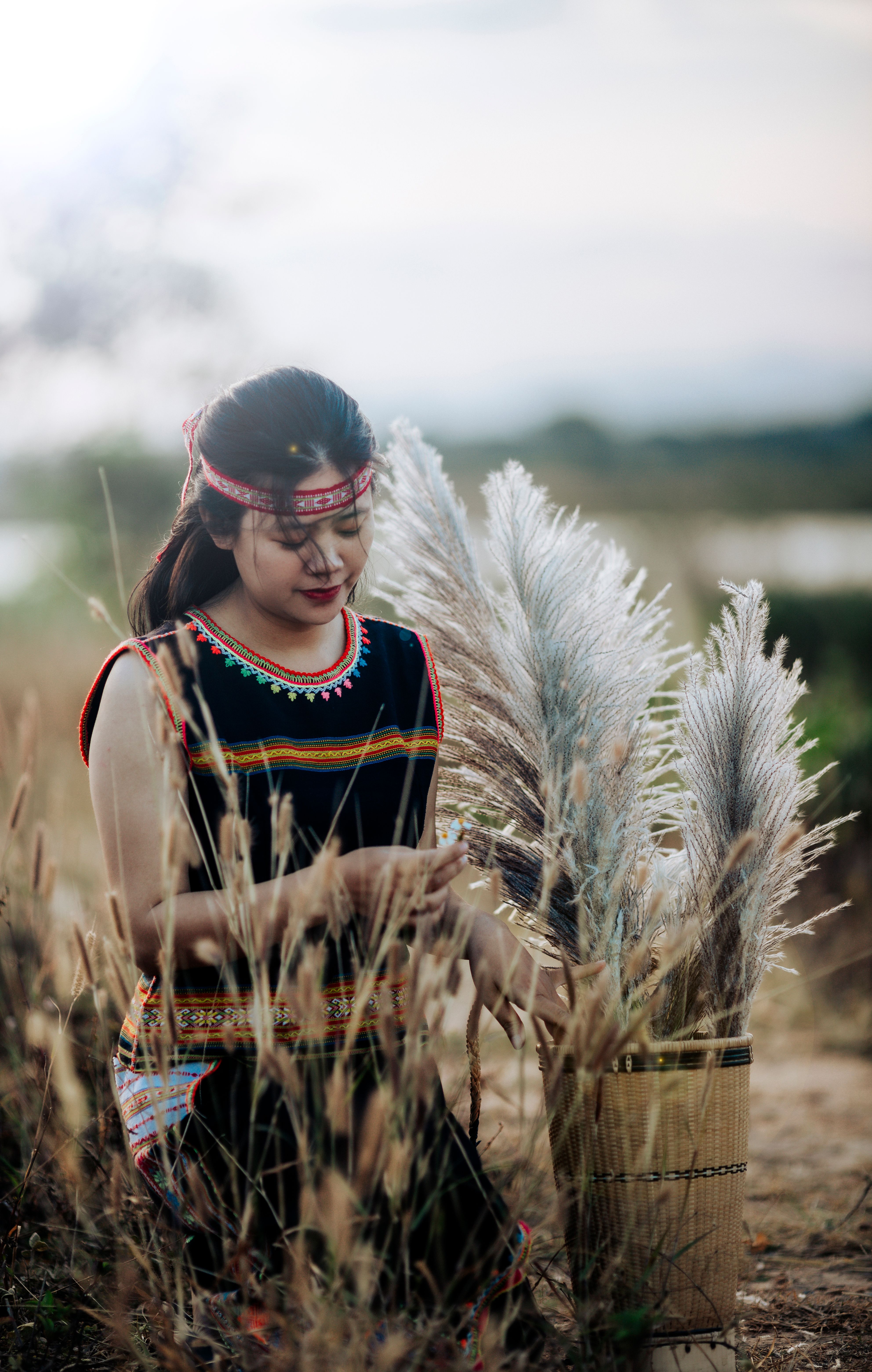 Traditional Vietnamese woman in ethnic attire harvesting pampas grass in a rural setting.