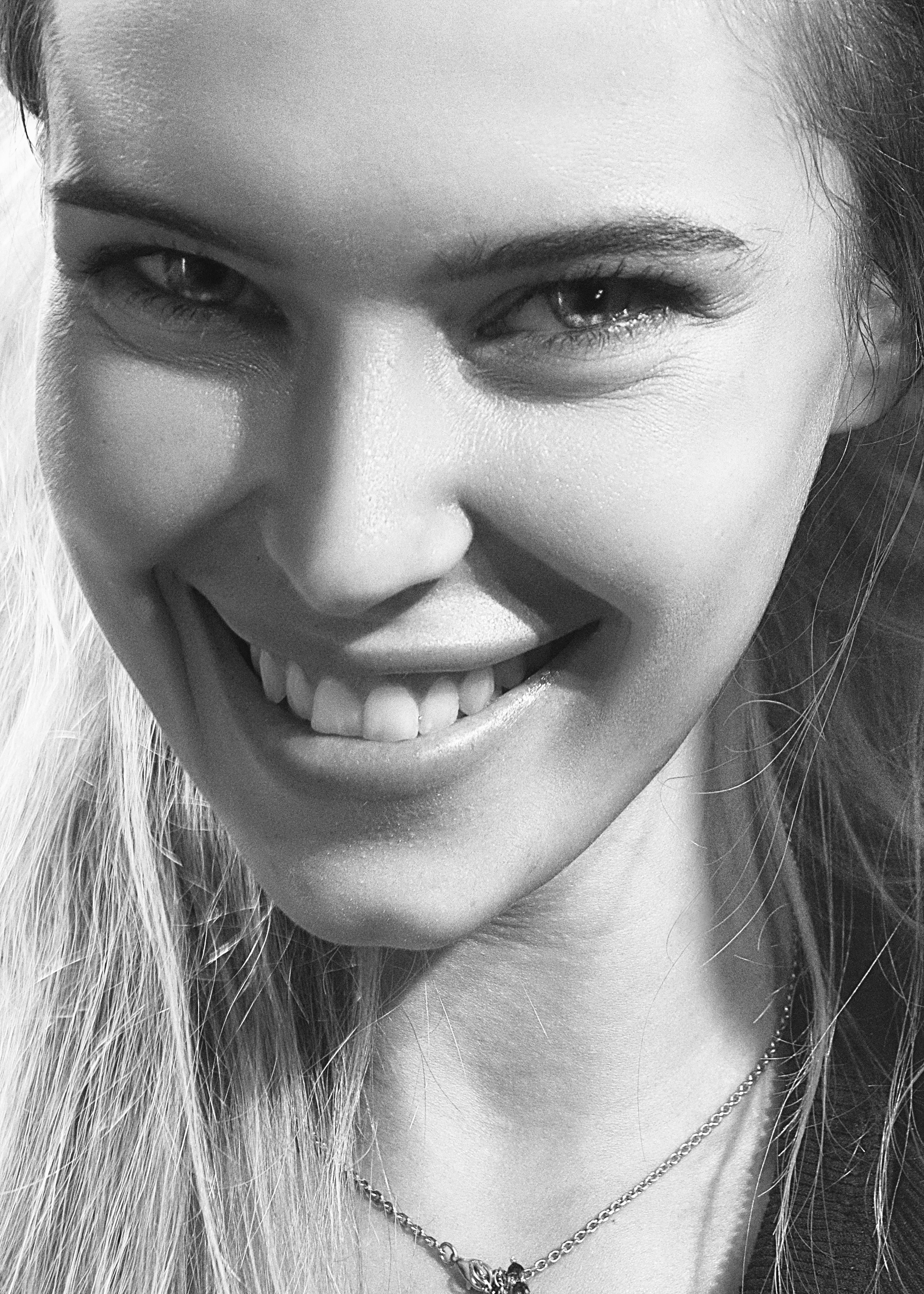Black and white close-up portrait of a smiling woman, capturing natural beauty.