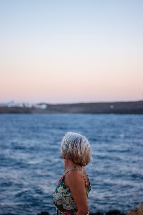 Free Senior woman gazing at ocean during sunset, serene moment by the sea. Stock Photo