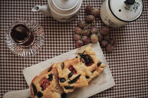 Free Top-down view of homemade focaccia bread arranged with tea and grapes on a rustic table setting. Stock Photo