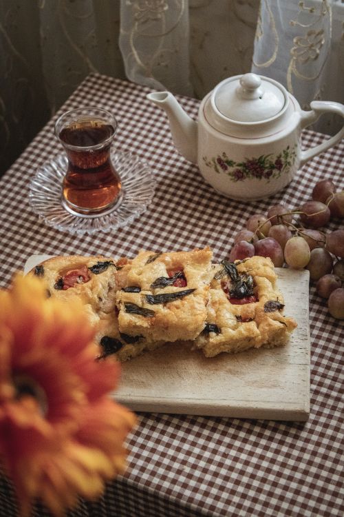 Free A warm, cozy indoor setup featuring tea, homemade focaccia, and grapes on a checkered tablecloth. Stock Photo