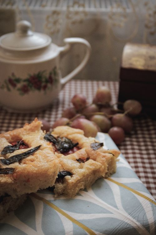 Free A cozy scene with rustic bread, grapes, and a floral teapot on a checkered tablecloth. Stock Photo