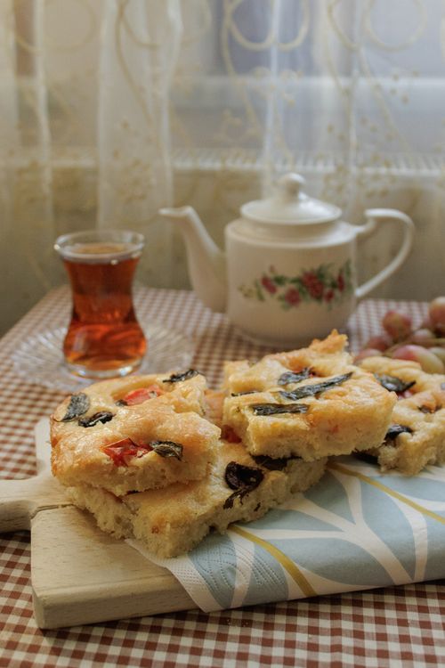 Free Cozy indoor setting featuring homemade focaccia bread, a teapot, tea, and grapes on a checkered table. Stock Photo