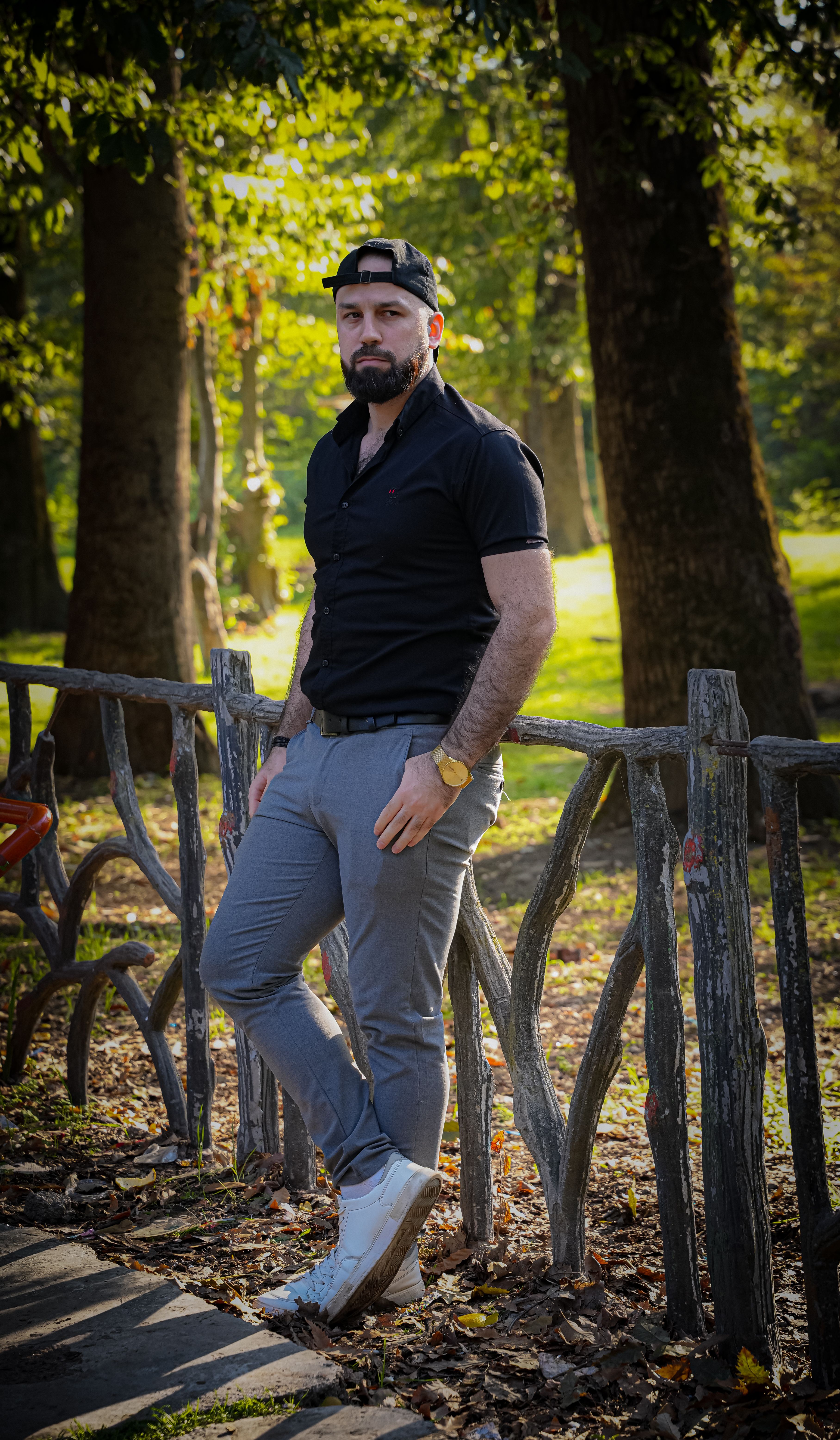 Man in black shirt and hat standing by a wooden fence in a sunny autumn park.