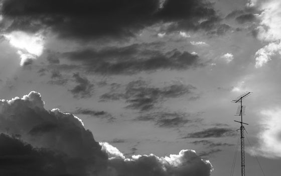 Dramatic black and white sky with clouds and antenna silhouette.