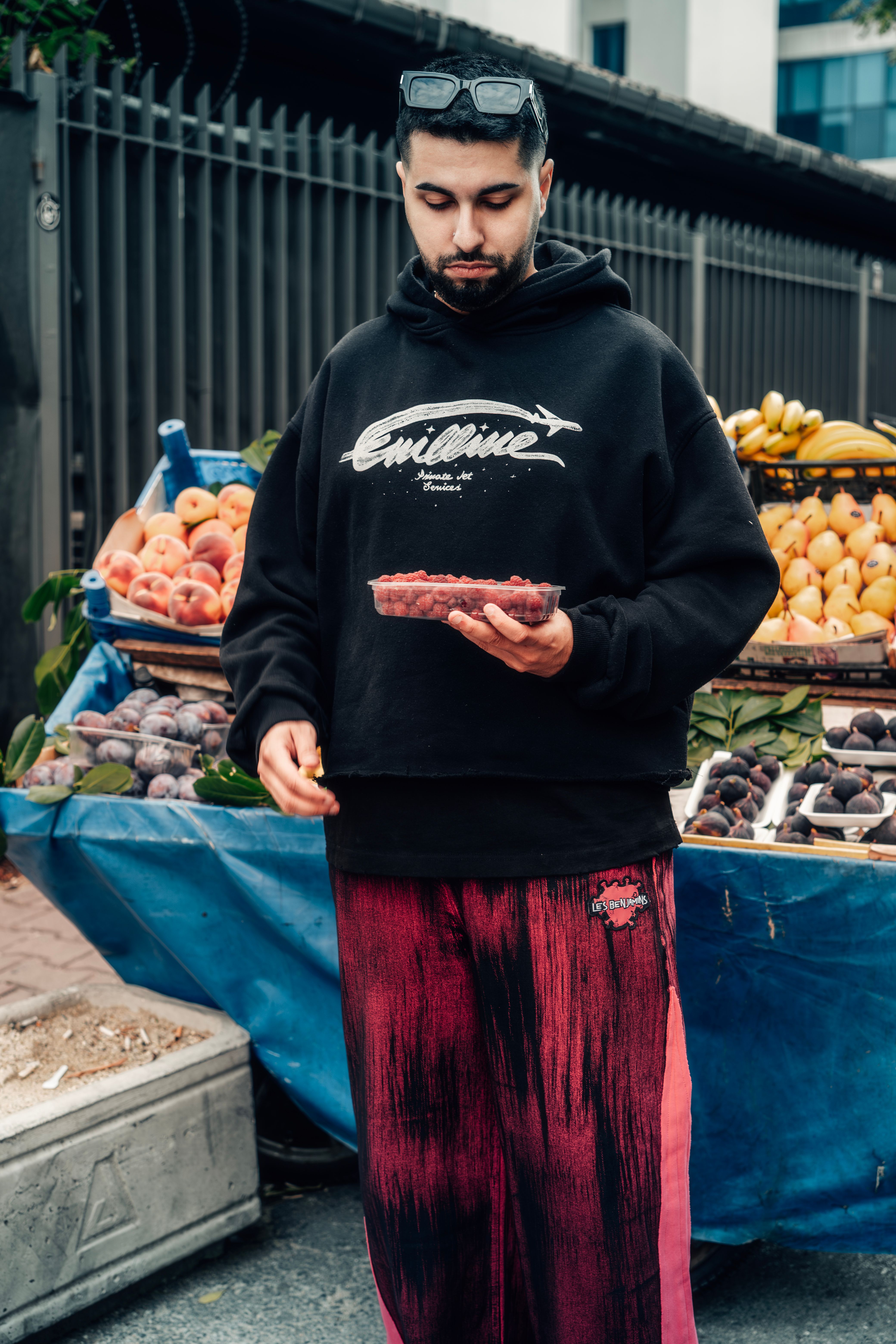 A man in casual attire selecting fresh fruits at a bustling outdoor market.