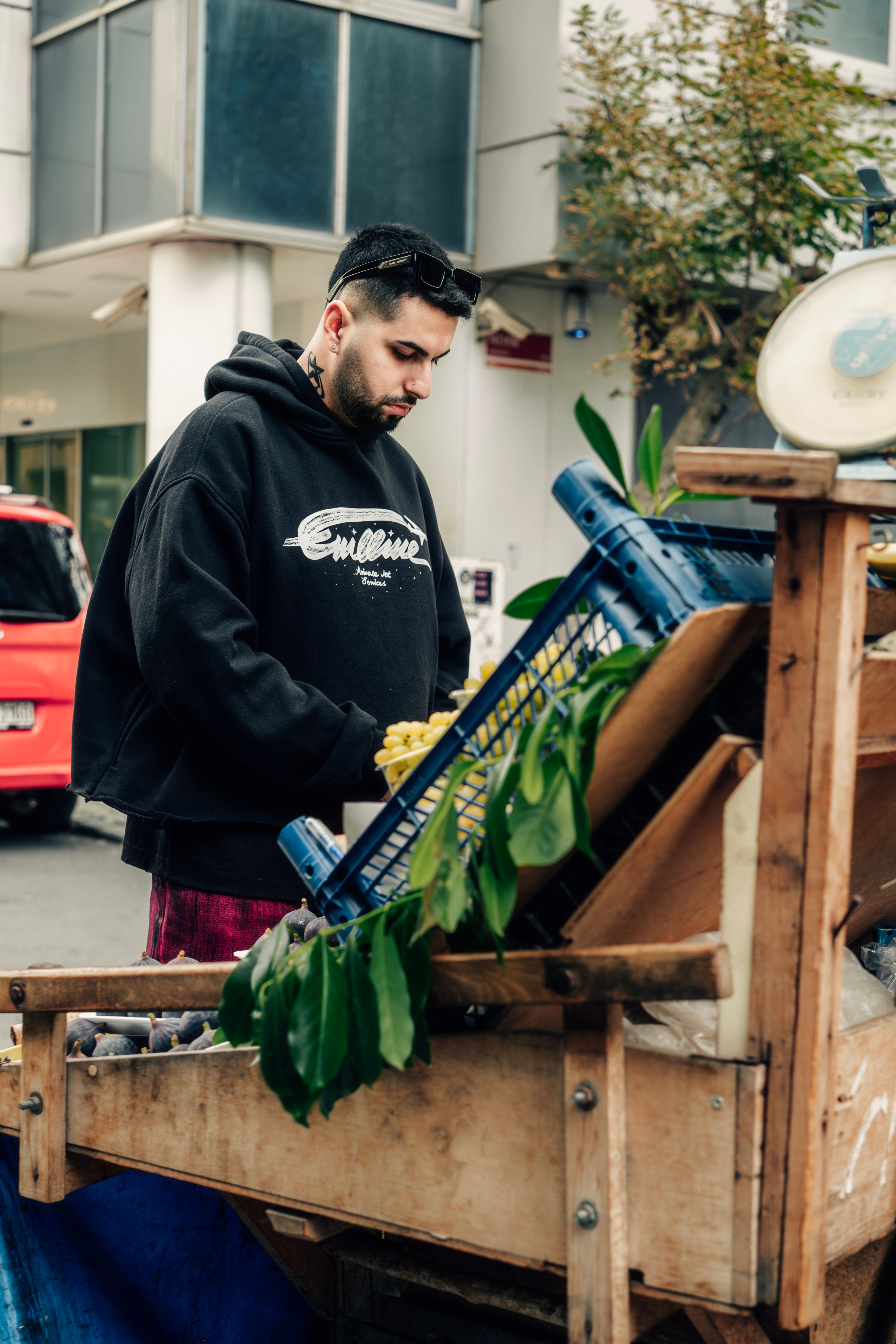 A street vendor sells fresh produce from a wooden cart on a city street.